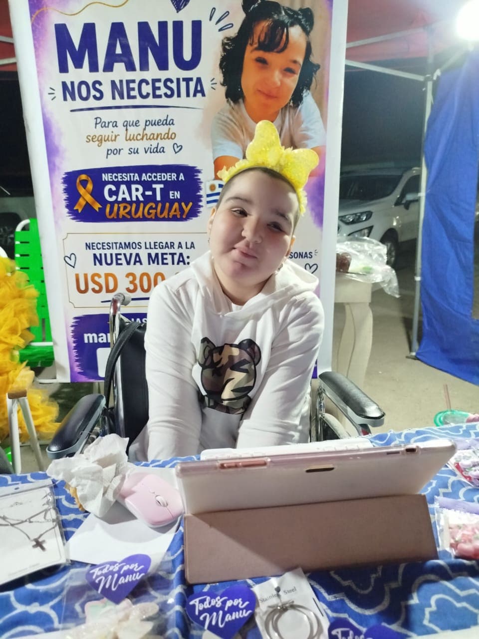 Manu en un puesto de la campaña, junto al cartel “Manu nos necesita”