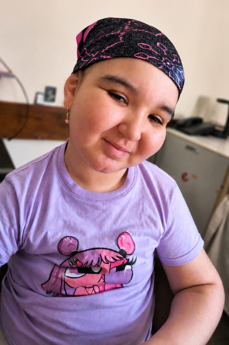 Manu sonriendo con un pañuelo y una remera lila